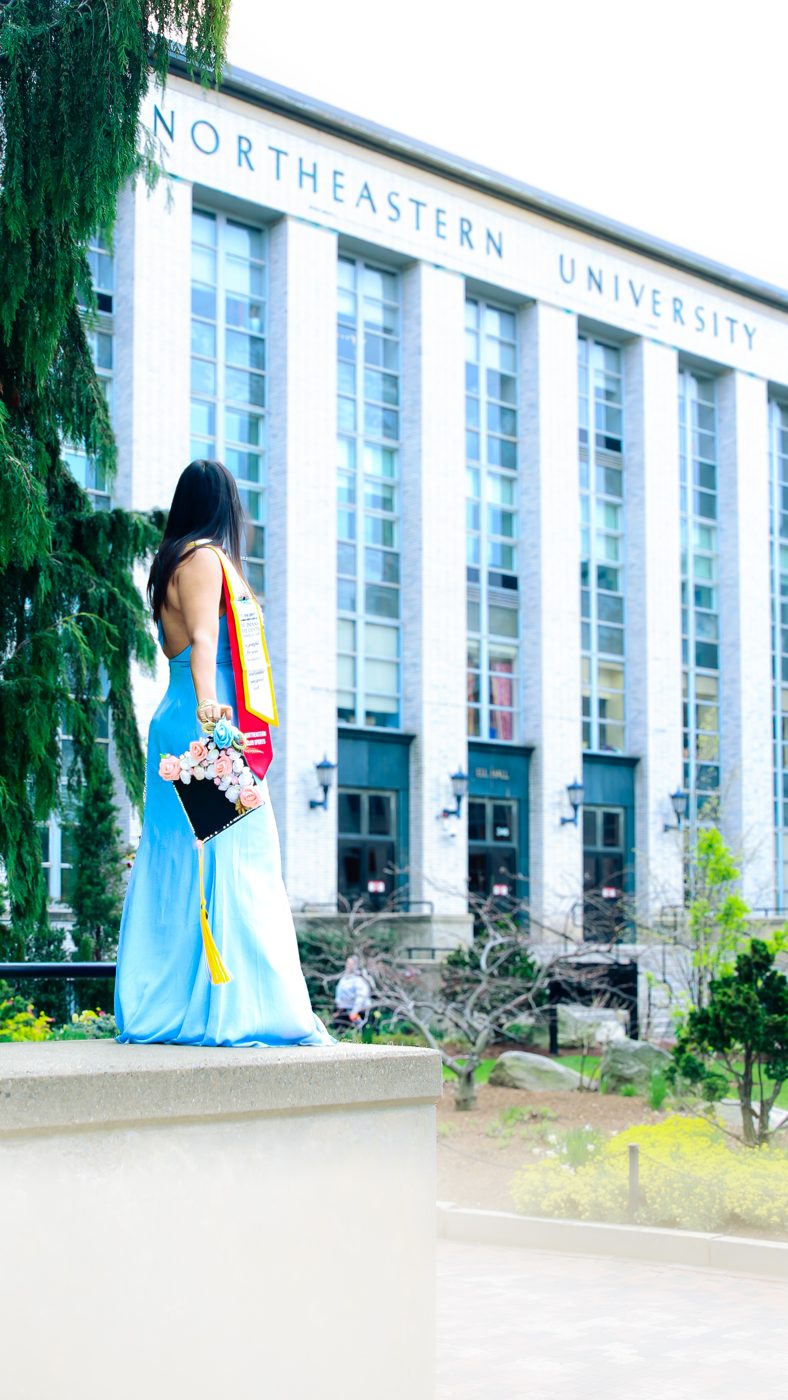 Graduate in a blue gown holding a flower-decorated cap, Northeastern University